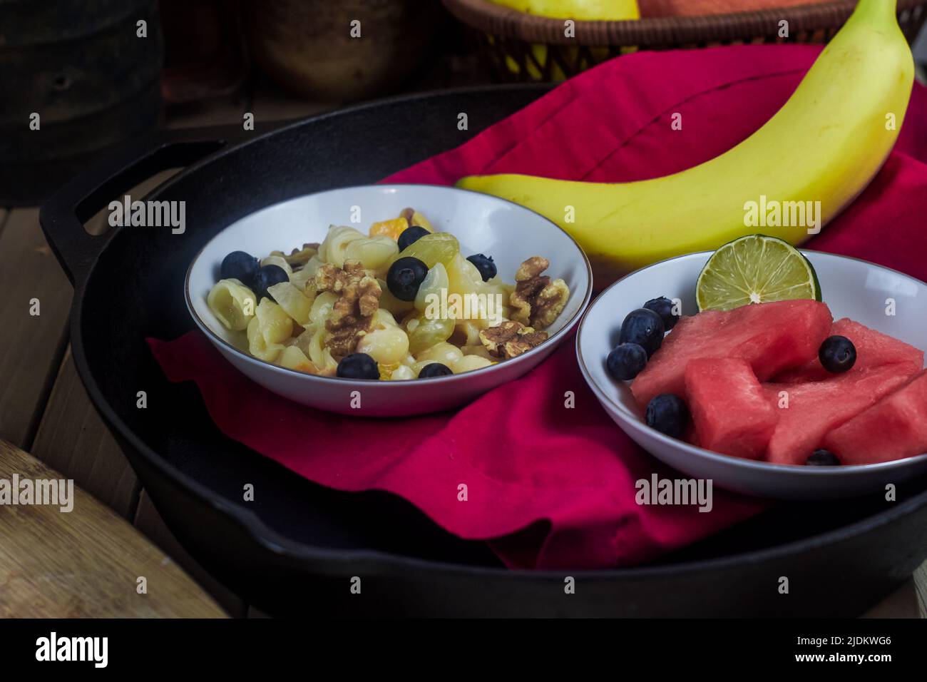 A fruit and nut salad with watermelon chunks, blueberries, a half lime, and a whole banana resting on a red linen napkin in a cast-iron skillet. Stock Photo