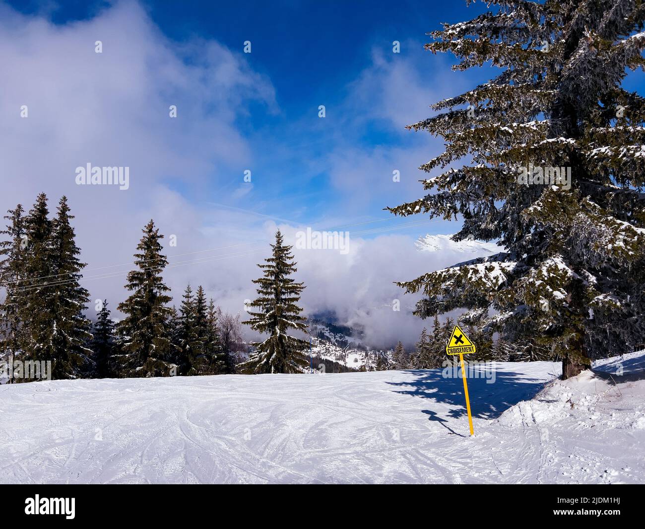 Ski track with crossing yellow sign over high altitude clouds Stock Photo