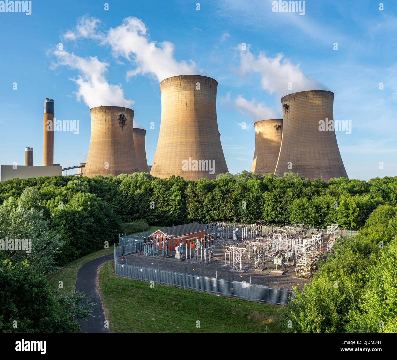 An aerial view of the cooling towers and chimney of a large coal fired power station generating electricity with electrical equipment to supply power Stock Photo