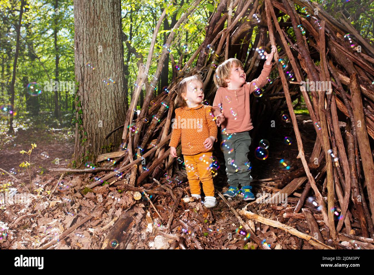 Two kids boy, girl play with soap bubbles in hut of branches Stock Photo