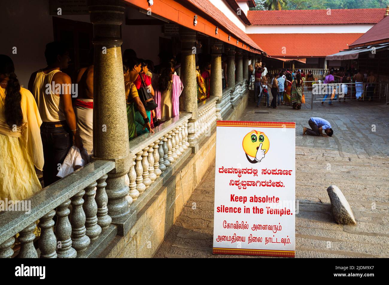 Dharmasthala, Karnataka, India : A row of pilgrims walks past a man kneeling before entering the Manjunatha Temple. Some 10.000 pilgrims pass through Stock Photo