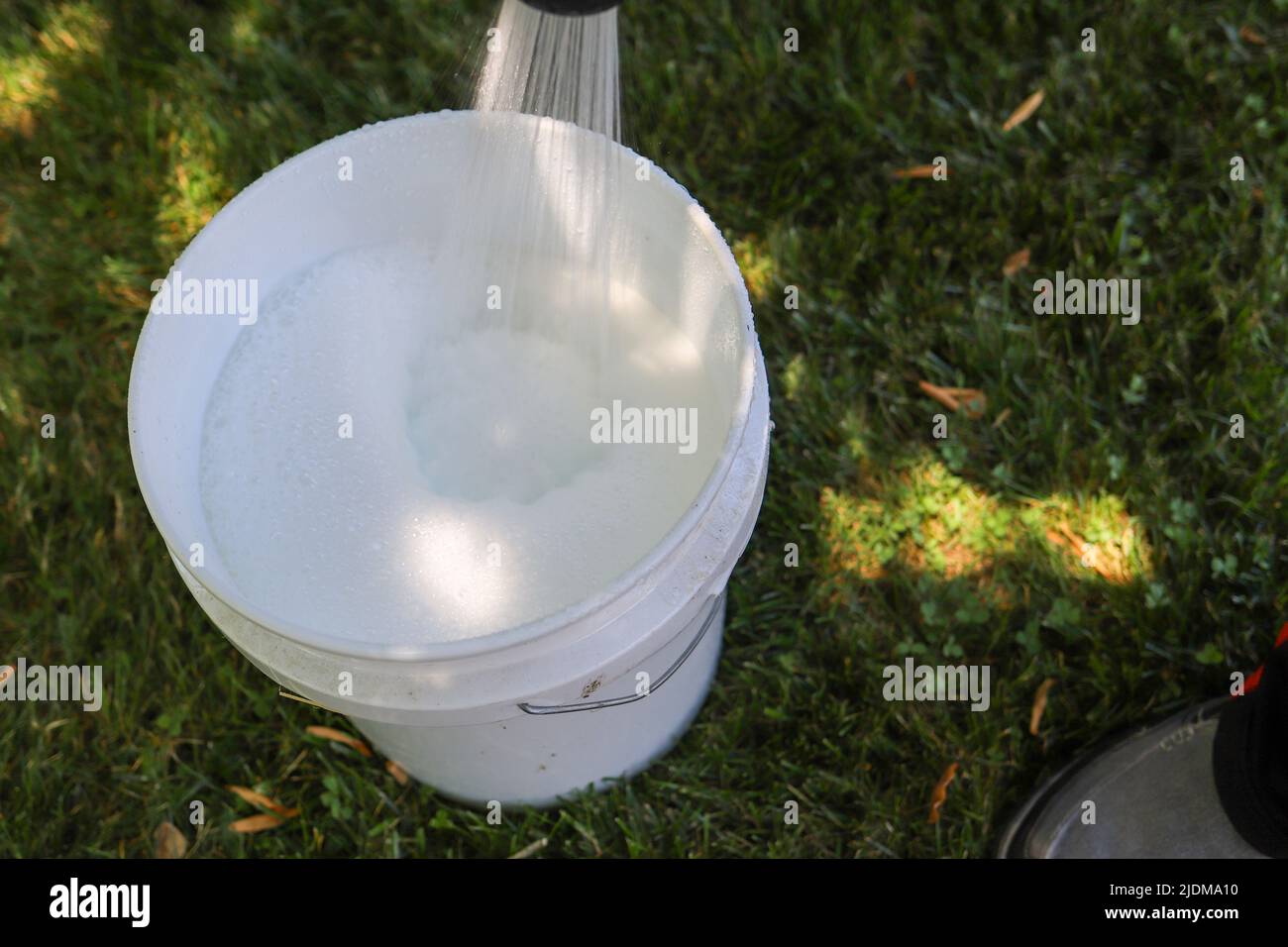 Close up of a person spraying water into a bucket of soapy water Stock Photo