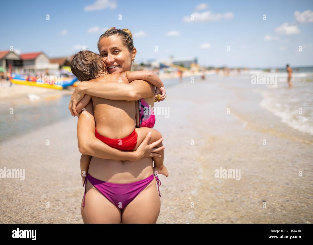 A caring kind beautiful mother in bright summer bikini, swimsuit is holding  a little cute baby who wants to sleep under the hot sun on the beach near  Stock Photo - Alamy