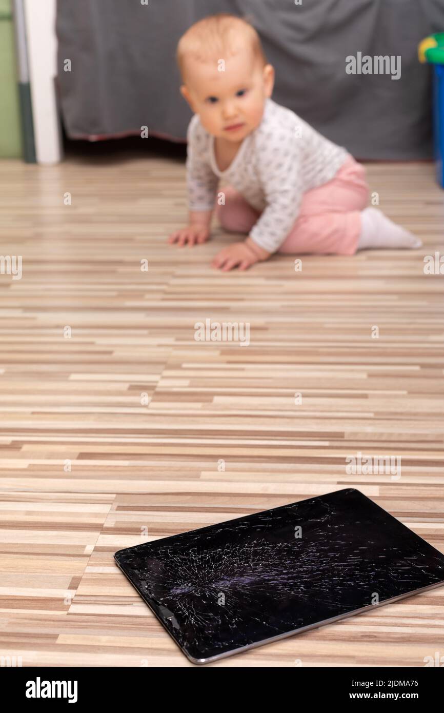 Broken tablet computer lying on a floor with cracked touch screen. Little baby who broke it is in background Stock Photo