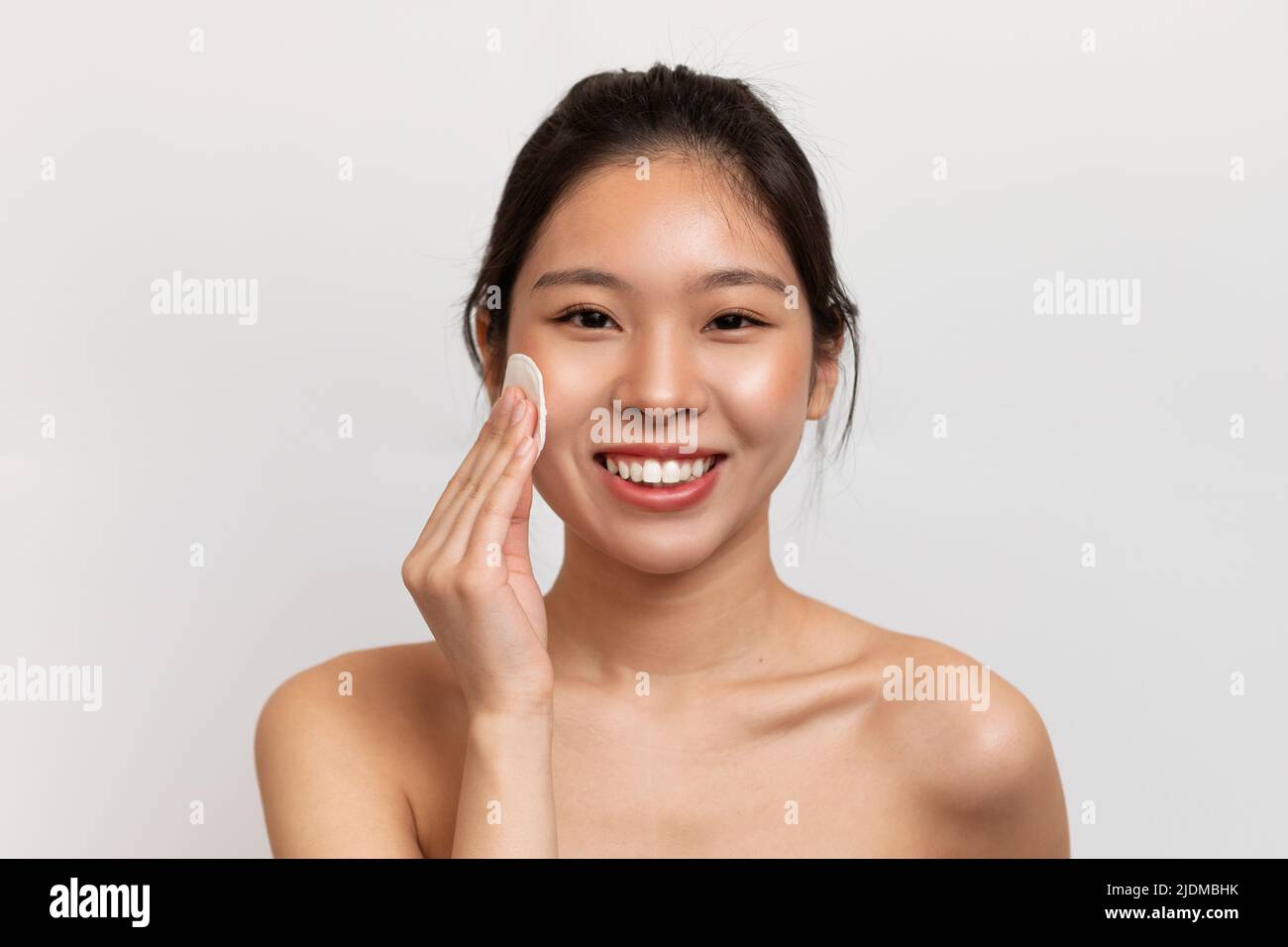 Skincare concept. Happy korean woman cleaning face with cotton pad