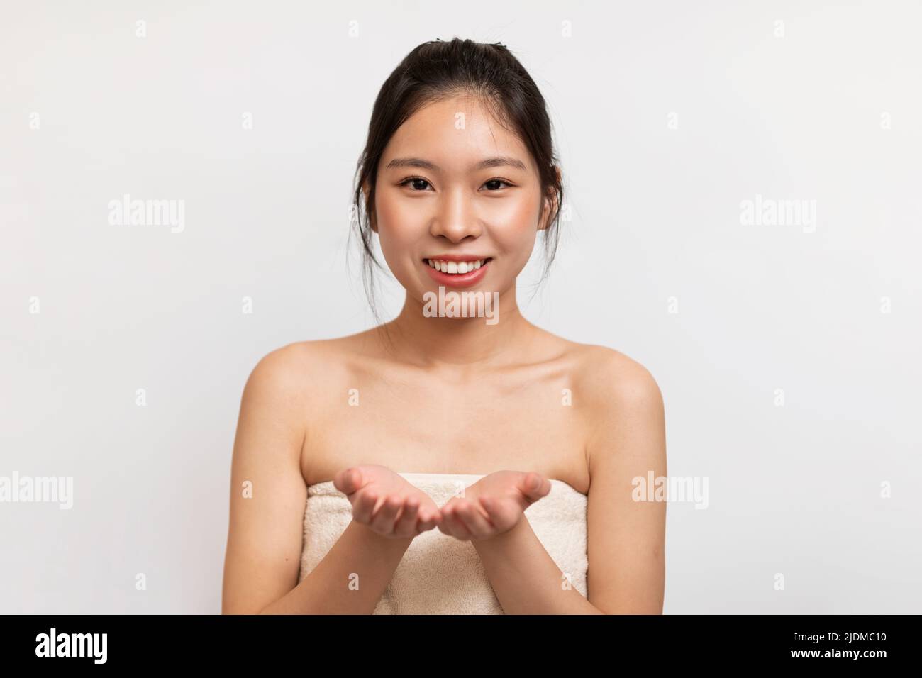 Happy young asian lady wrapped in bath towel demonstrating something on empty palms, showing invisible object Stock Photo