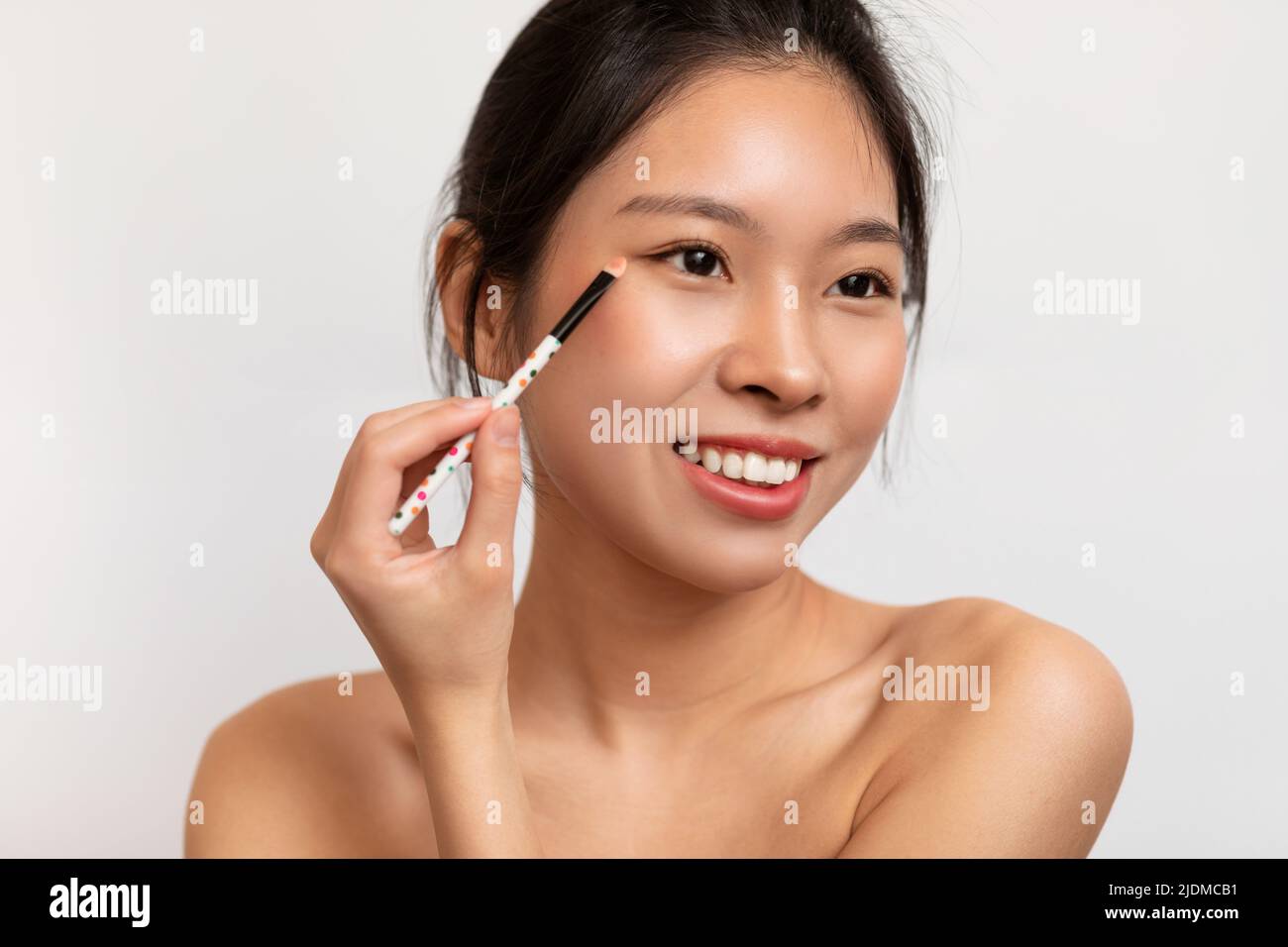 Portrait of lovely young asian lady applying eye shadow on her face