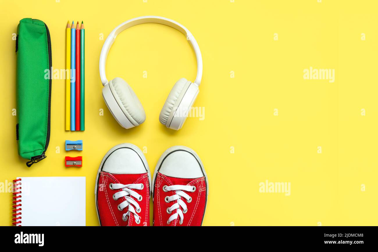 Top view of red sneakers, pencil case, headphones and school supplies with space for text on yellow background. Back to school concept Stock Photo