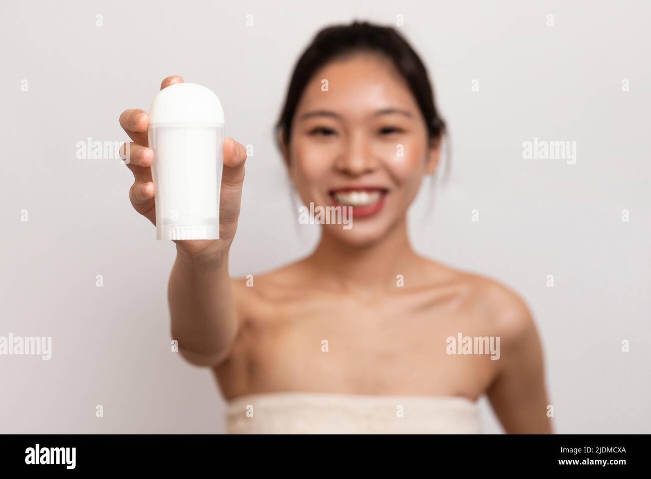 Personal hygiene and treatment after shower. Happy young asian lady in towel showing deodorant