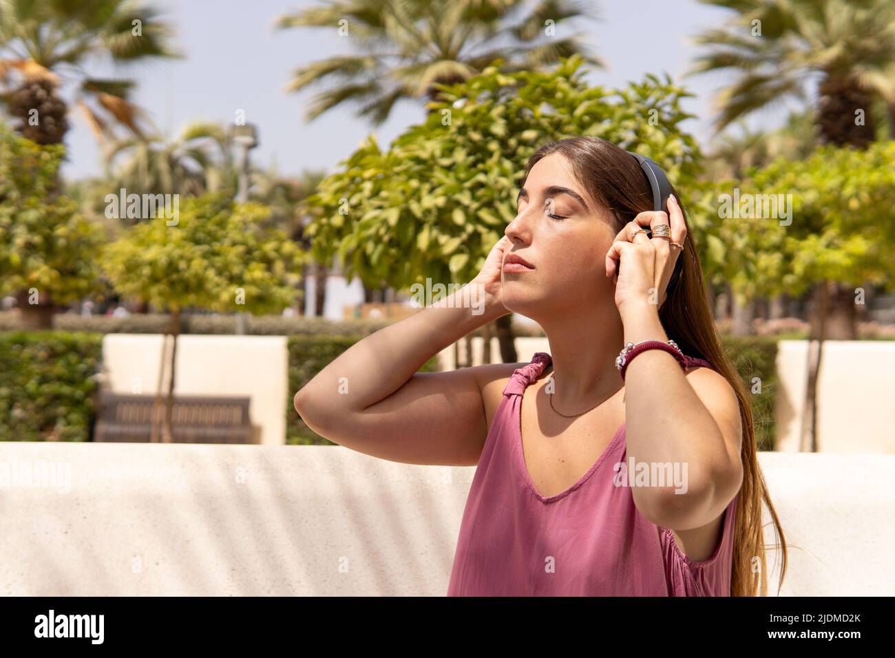 Pretty girl in pink dress sitting on a park bench listening to music
