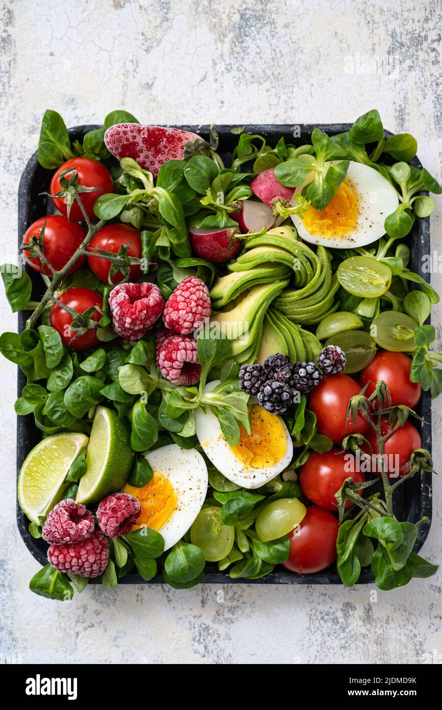 Vegetables salad on a tray raspberries , avocado , tomatoes , egg , radish , blackberries Stock Photo