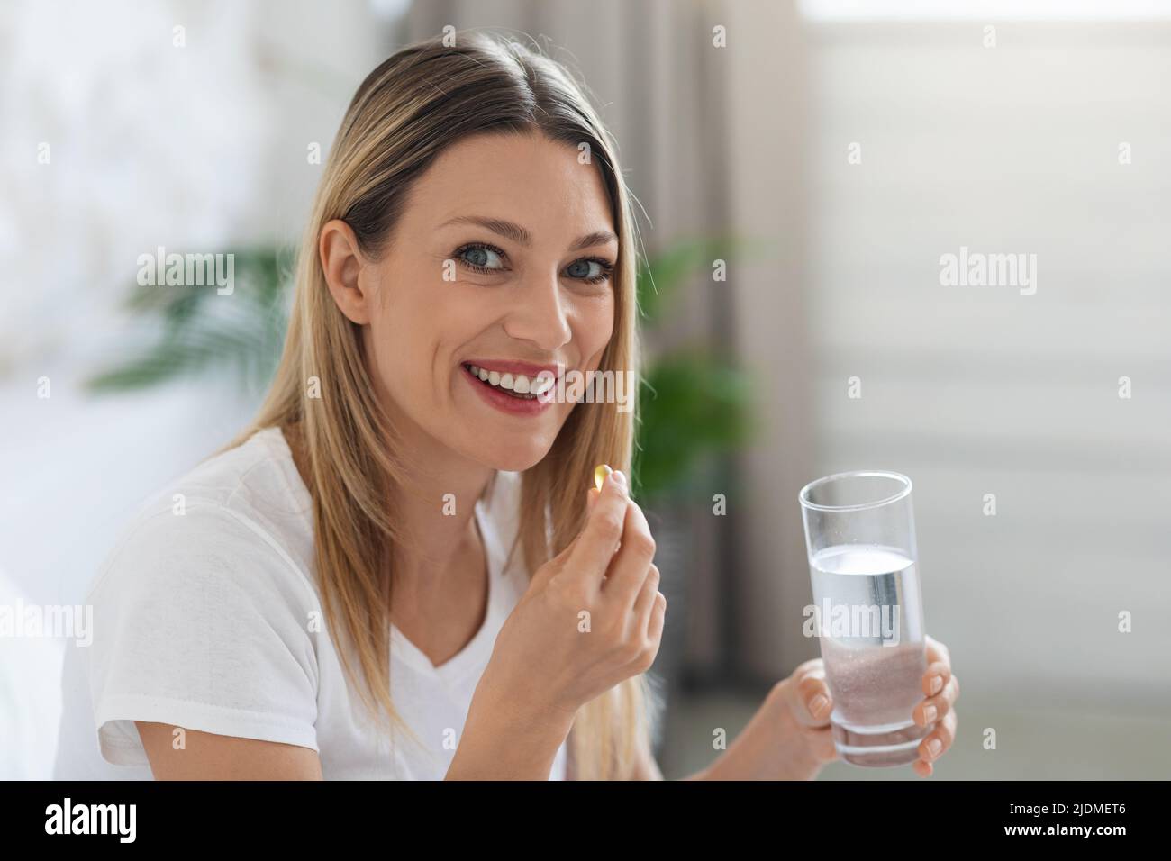 Smiling pretty woman taking pill after waking up Stock Photo