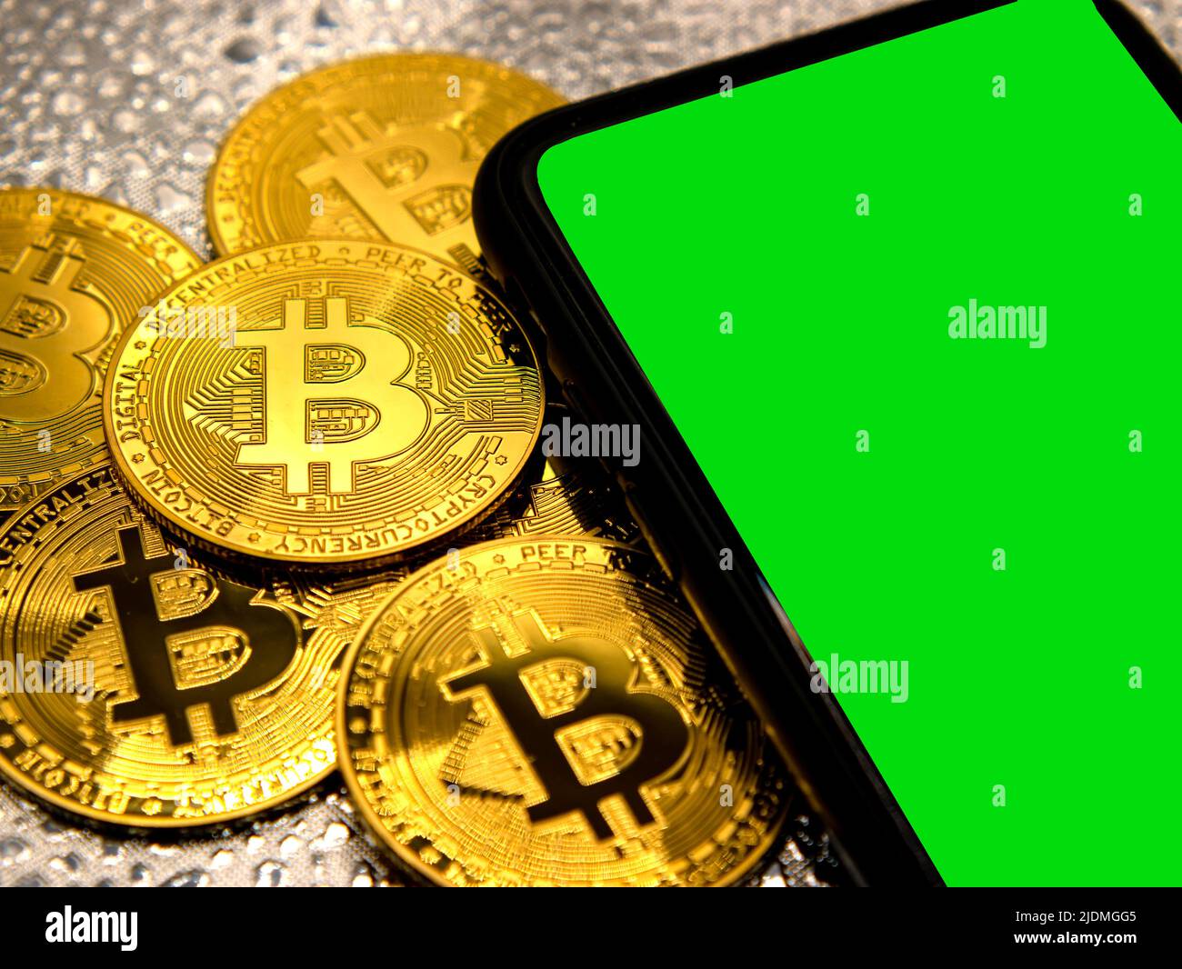 Bitcoin coins in golden metal with a smarthphone beside it, green screen area copy space Stock Photo