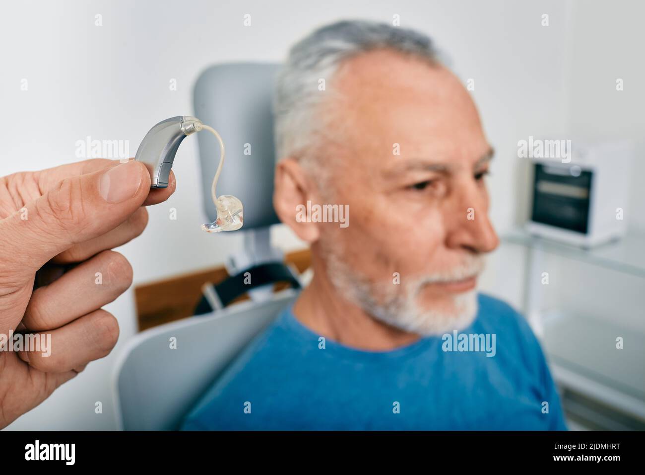 Audiologist presents BTE hearing aid for mature hearing impaired man to treat his deafness, close-up. Audiology, auditory solutions Stock Photo