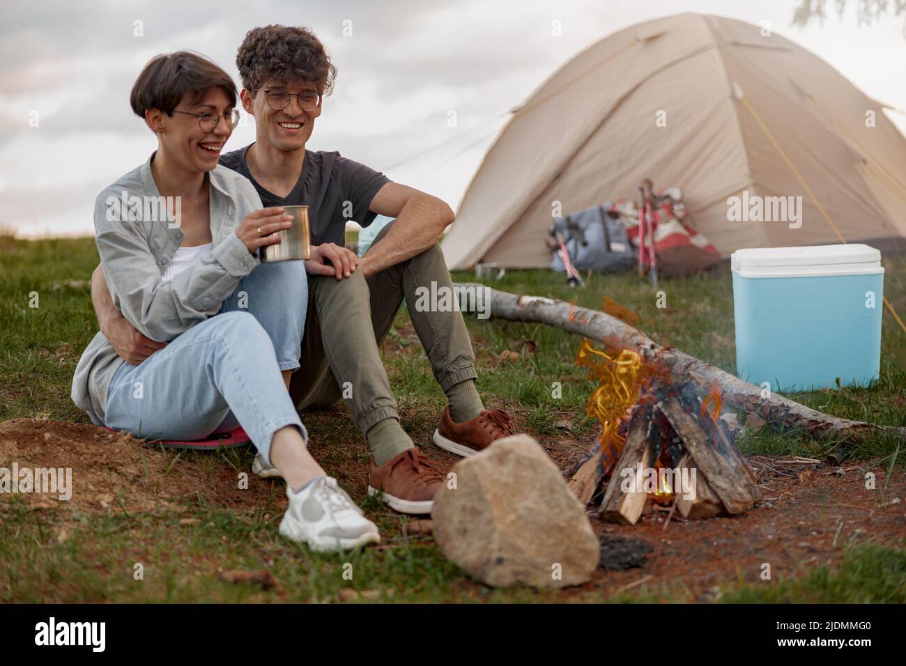 Man and woman drinking tea or coffee at fire in camp stop. Enjoying