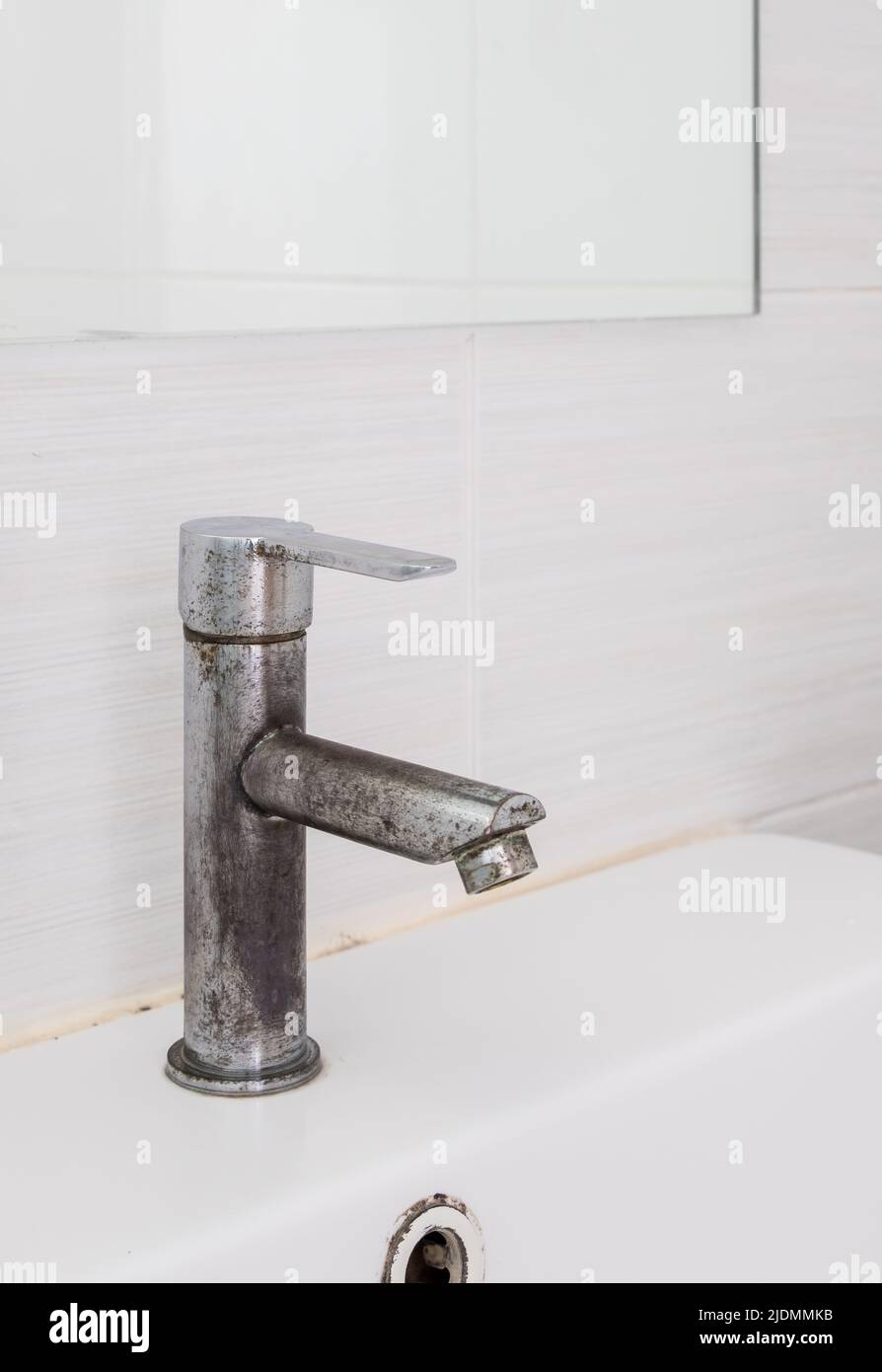 The ceramic sink basin with the stained faucet near the clear mirror on the white tile wall of the restroom in the city house, front view with the cop Stock Photo