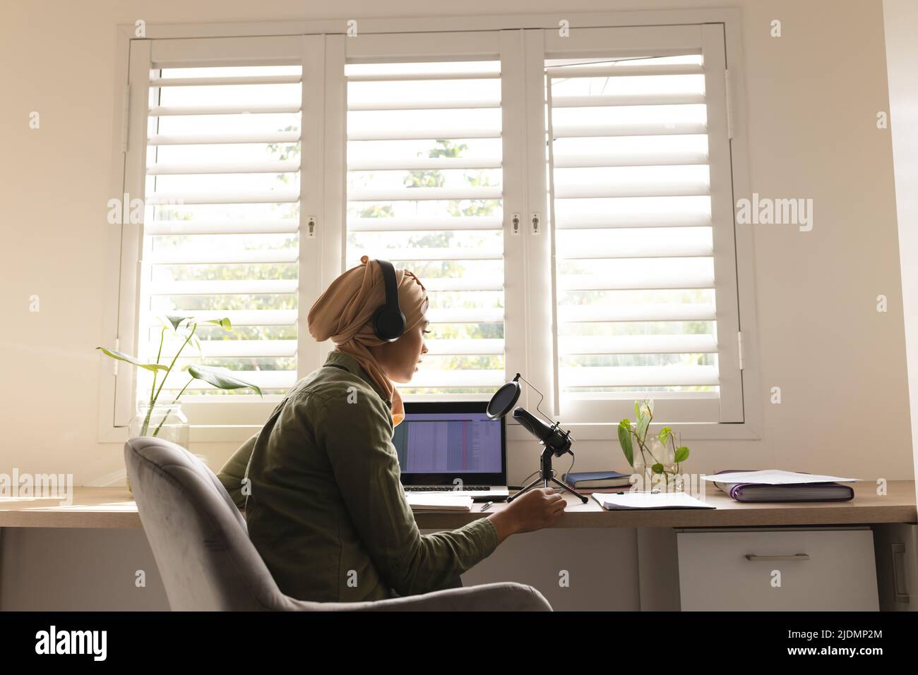 Biracial young woman in hijab recording podcast through condenser microphone at home studio Stock Photo