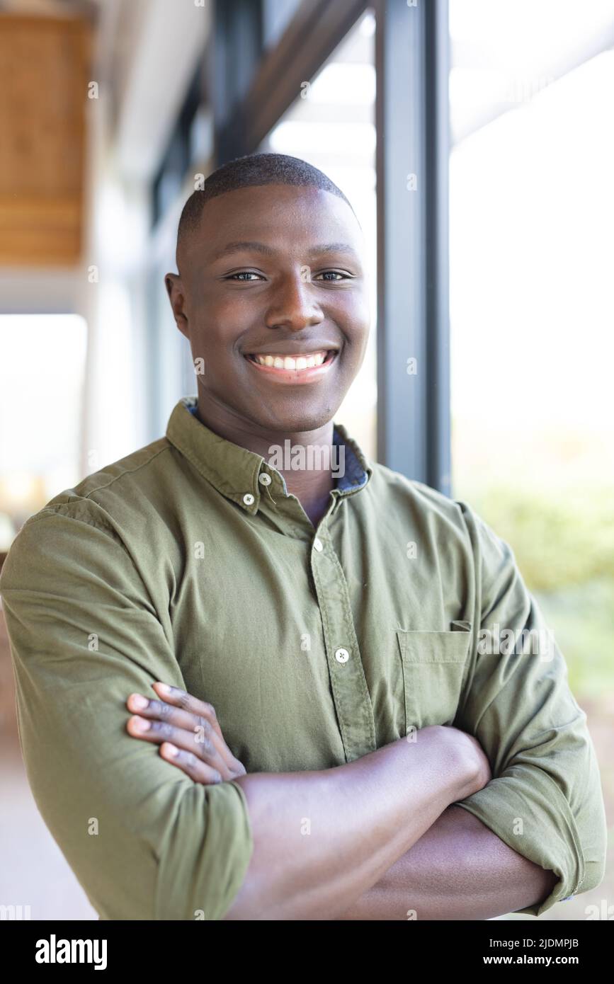 Portrait of smiling african american mid adult man with arms crossed standing by window at home Stock Photo