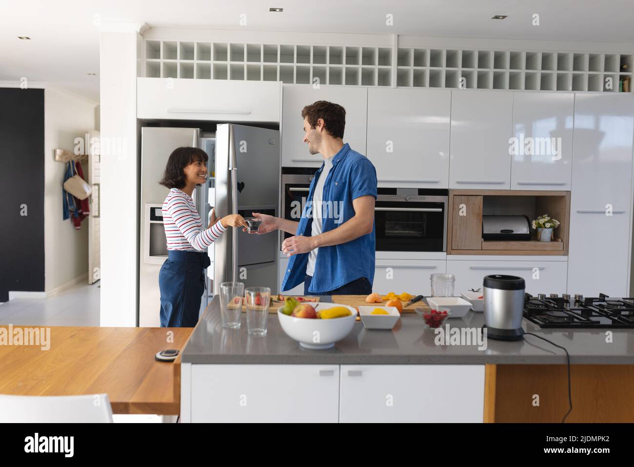 Asian girlfriend giving fruits from refrigerator to caucasian boyfriend making smoothie in kitchen Stock Photo