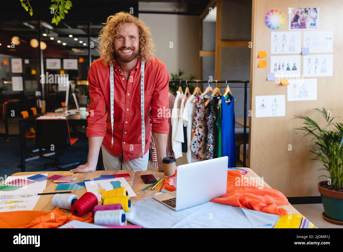 Portrait of smiling caucasian male fashion designer leaning at desk in studio office Stock Photo