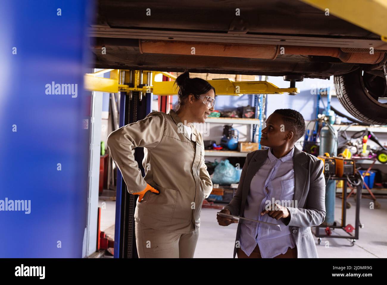 Multiracial mid adult female engineers discussing work under car lift in workshop, copy space Stock Photo