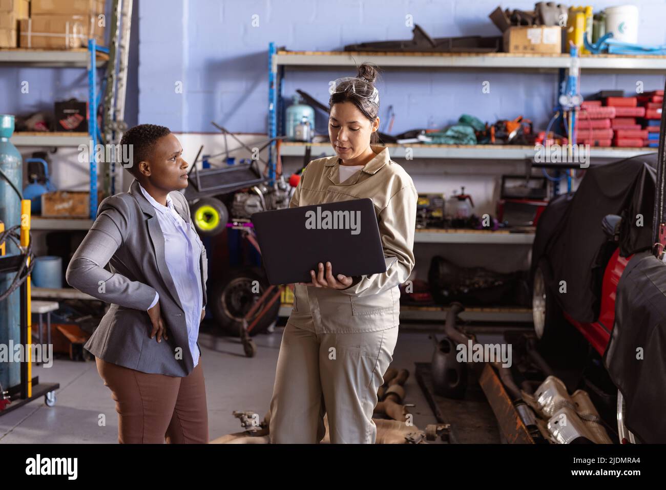 Confident multiracial mid adult female welders using laptop while working in workshop, copy space Stock Photo