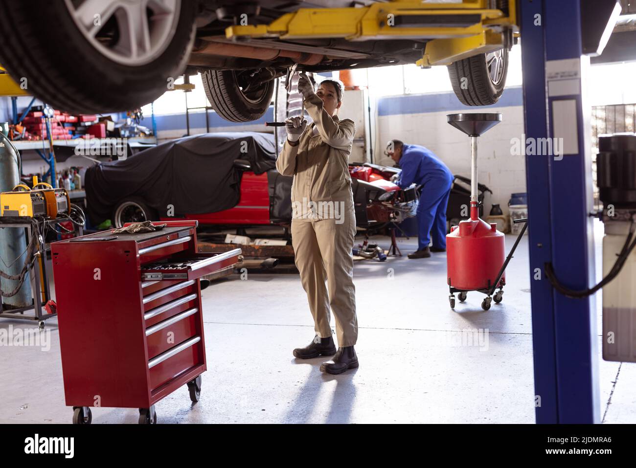 Mid adult female asian welder repairing car on lift in workshop, copy space Stock Photo