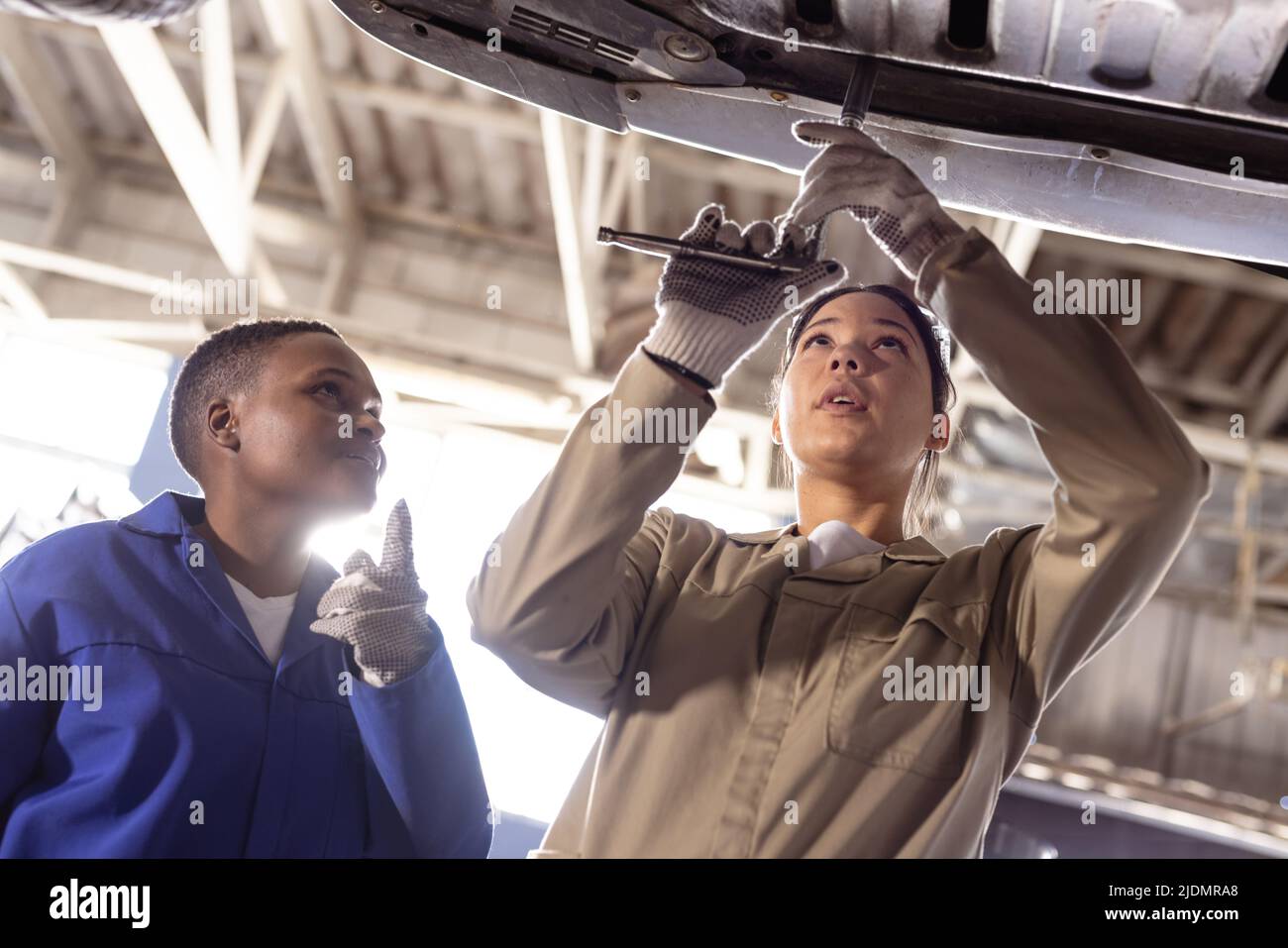 African american mid adult engineer assisting female asian colleague in repairing car Stock Photo
