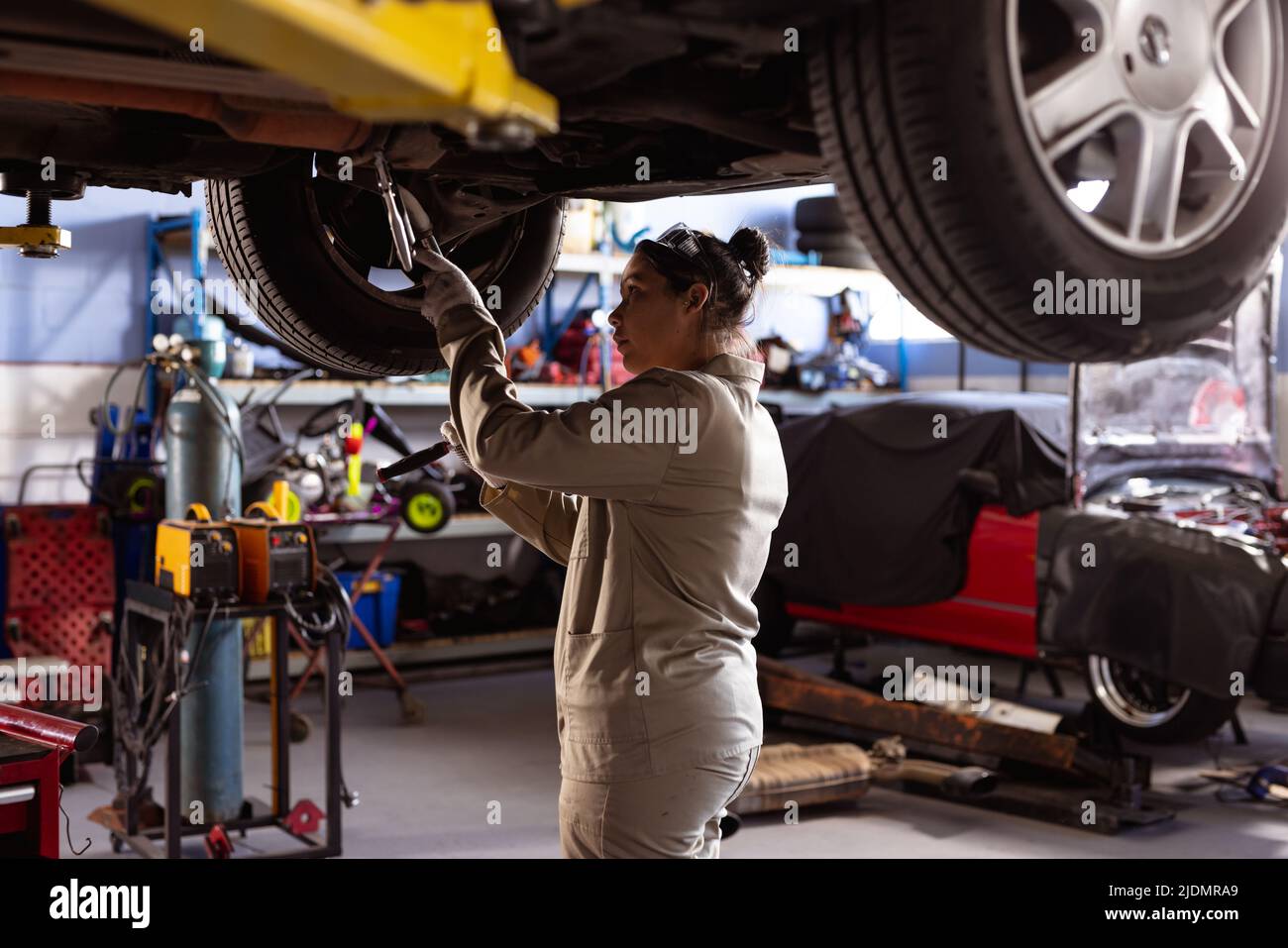 Side view of mid adult asian female technician using work tool while repairing car in workshop Stock Photo