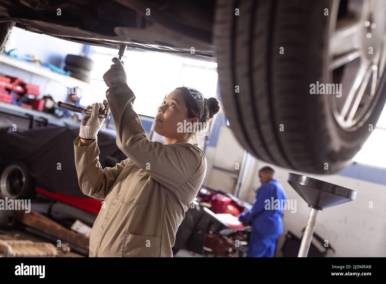 Asian mid adult female mechanic using wrench while repairing car in workshop Stock Photo