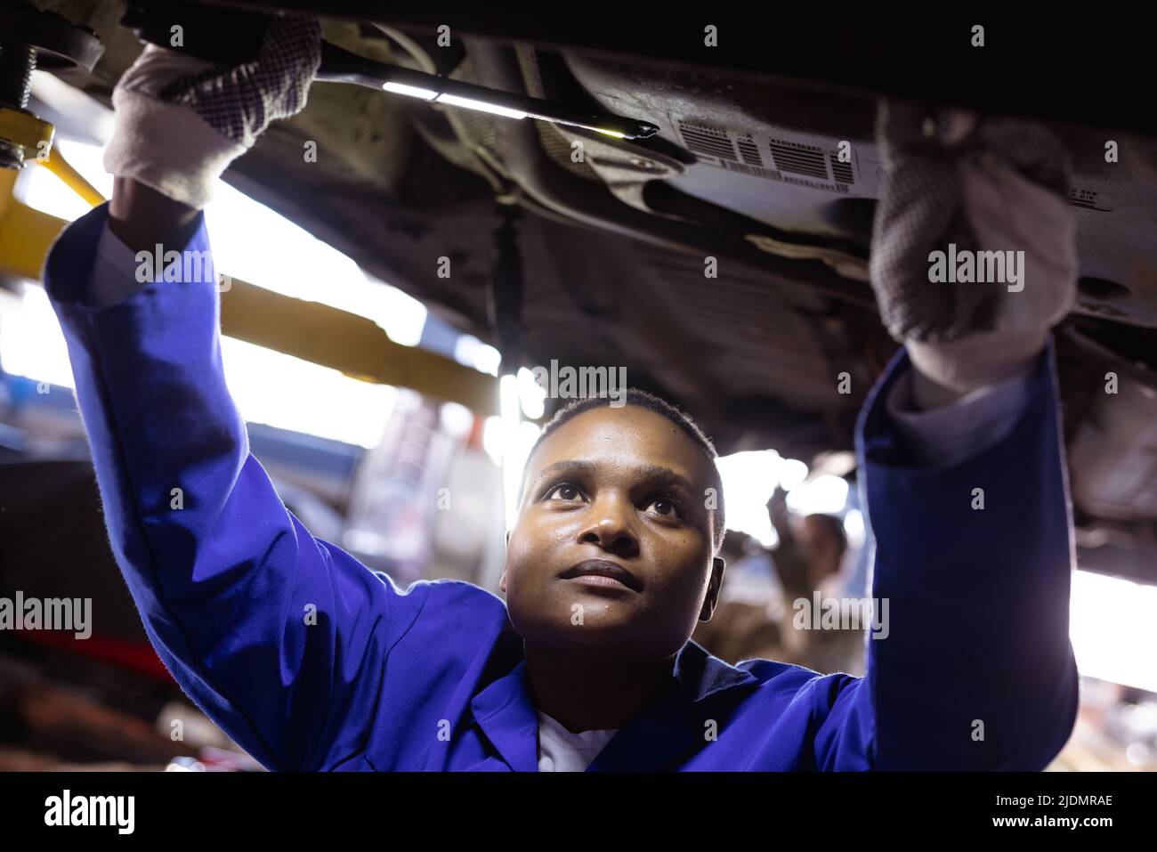 African american mid adult female engineer repairing car under car lift in workshop Stock Photo