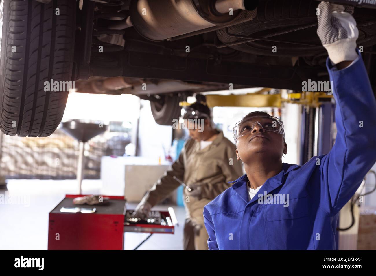 Multiracial mid adult female welders using work tools while repairing car on car lift in workshop Stock Photo