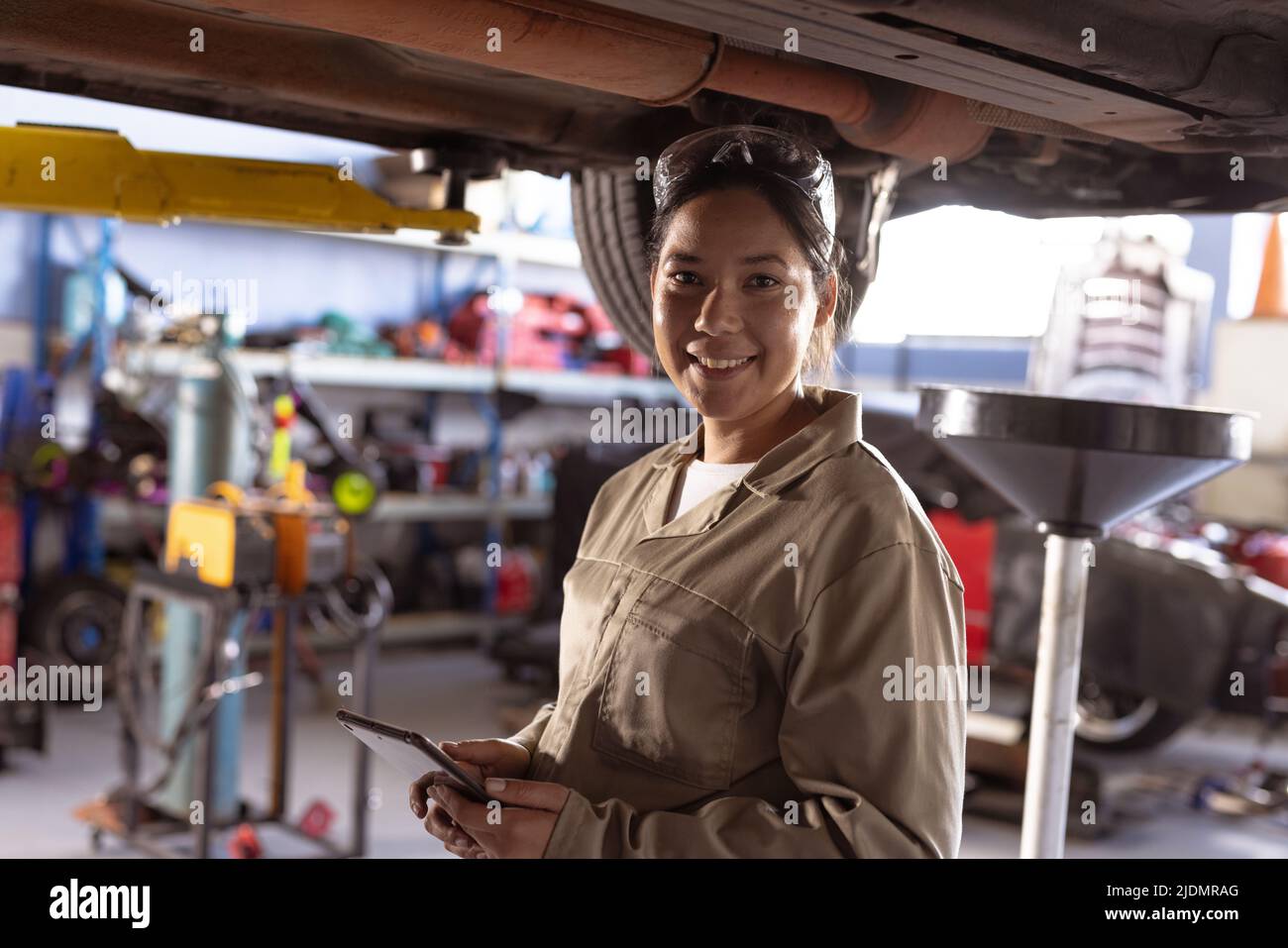 Portrait of smiling mid adult asian mechanic repairing car using digital tablet in workshop Stock Photo