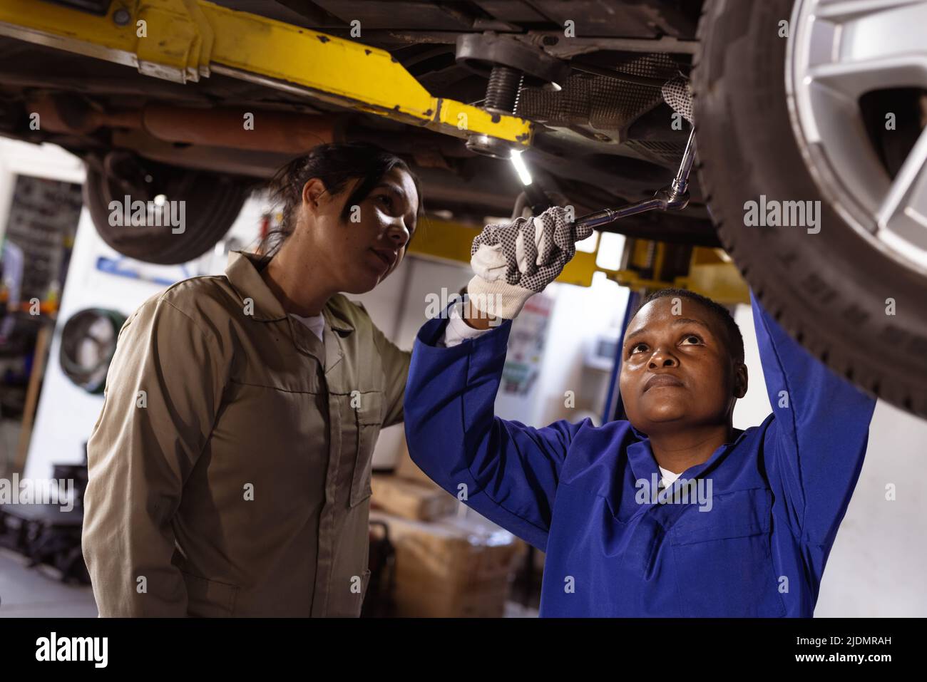 Asian female mechanic helping african american mid adult colleague in repairing car at workshop Stock Photo