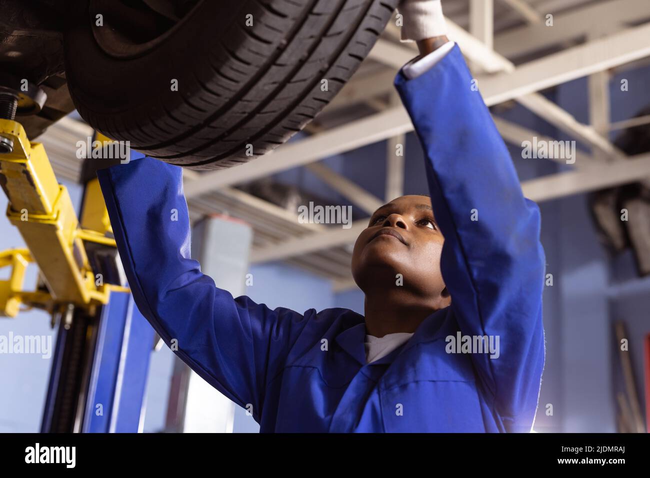 African american mid adult female mechanic examining car's tire in workshop Stock Photo