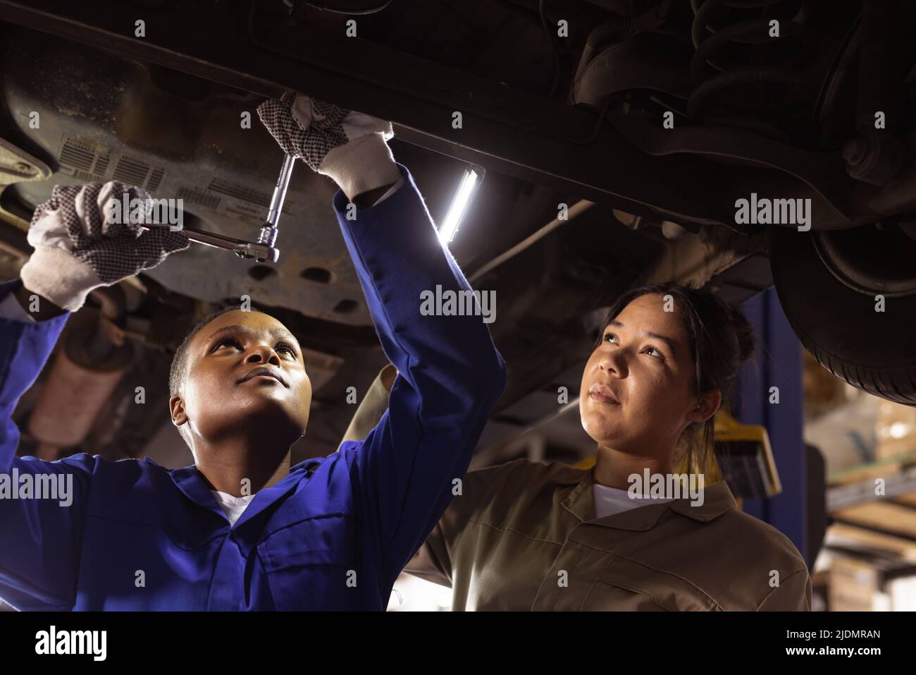 Mid adult asian female engineer assisting african american colleague in repairing car at workshop Stock Photo