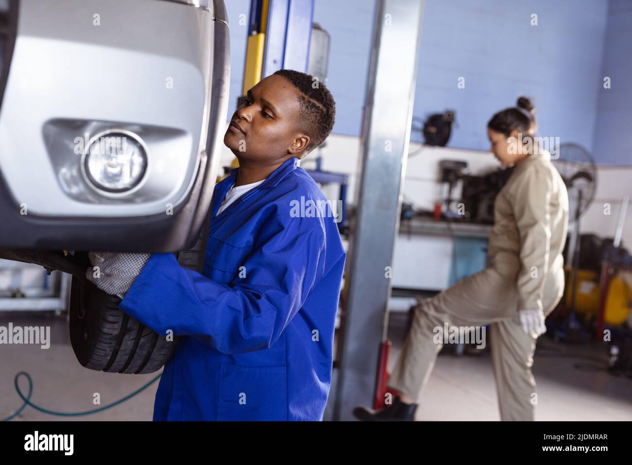 African american mid adult female mechanic repairing car with asian colleague working in background Stock Photo