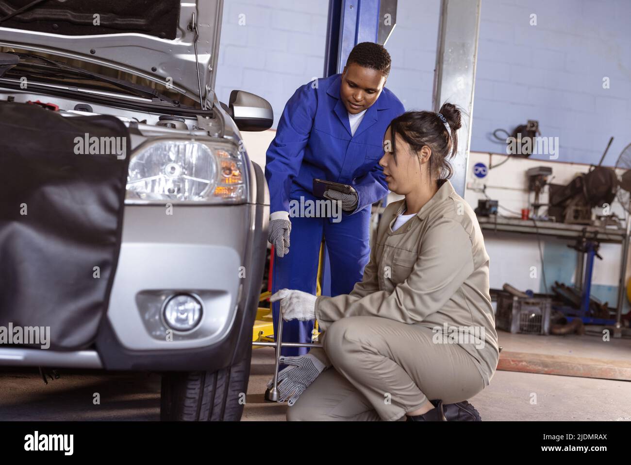 African american female engineer helping mid adult asian coworker in repairing at workshop Stock Photo