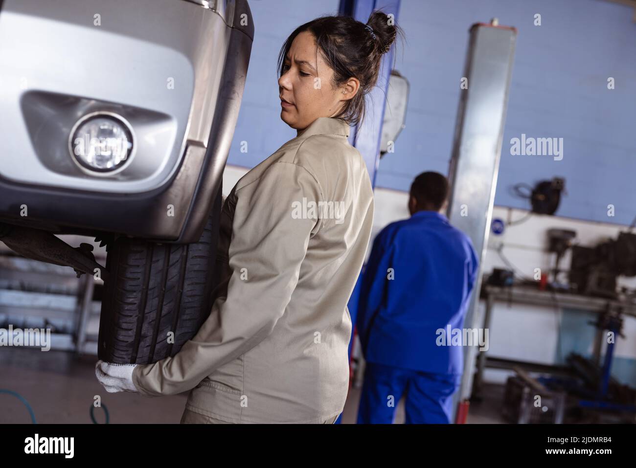 Mid adult asian female mechanic fixing car's tire in workshop with colleague in background Stock Photo