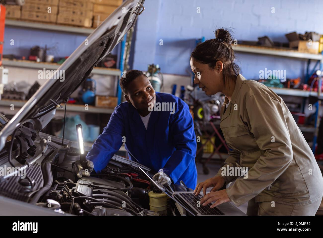 Mid adult multiracial female engineers examining car's engine while using laptop Stock Photo