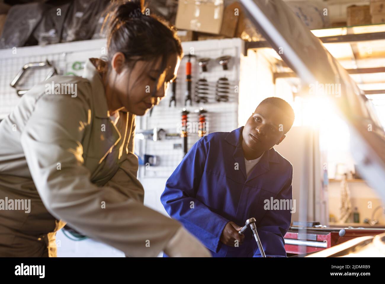 Mid adult female multiracial mechanics working together while repairing car in workshop Stock Photo