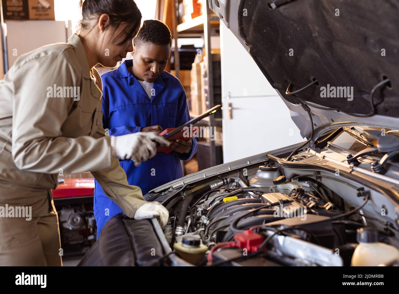 Mid adult multiracial female mechanics using digital tablet while repairing car's engine Stock Photo