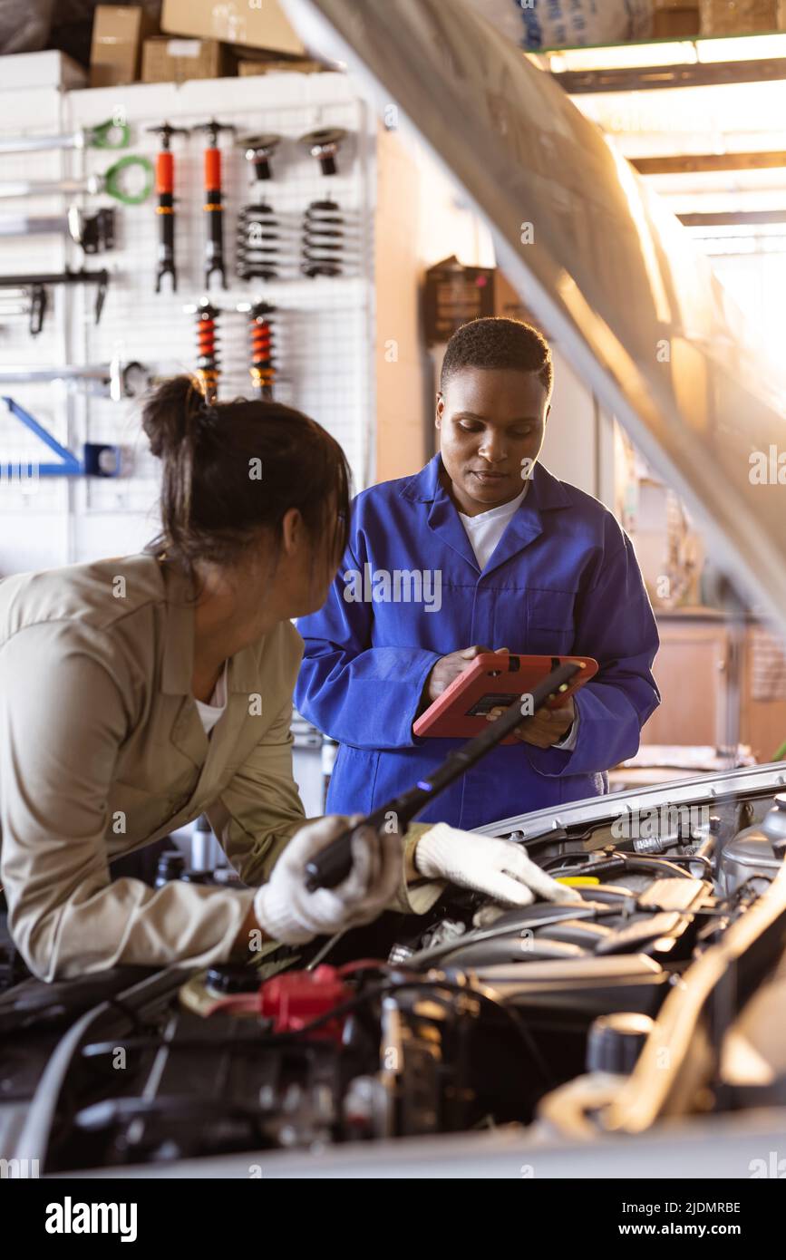 African american mid adult female welder with digital tablet assisting asian colleague in repairing Stock Photo