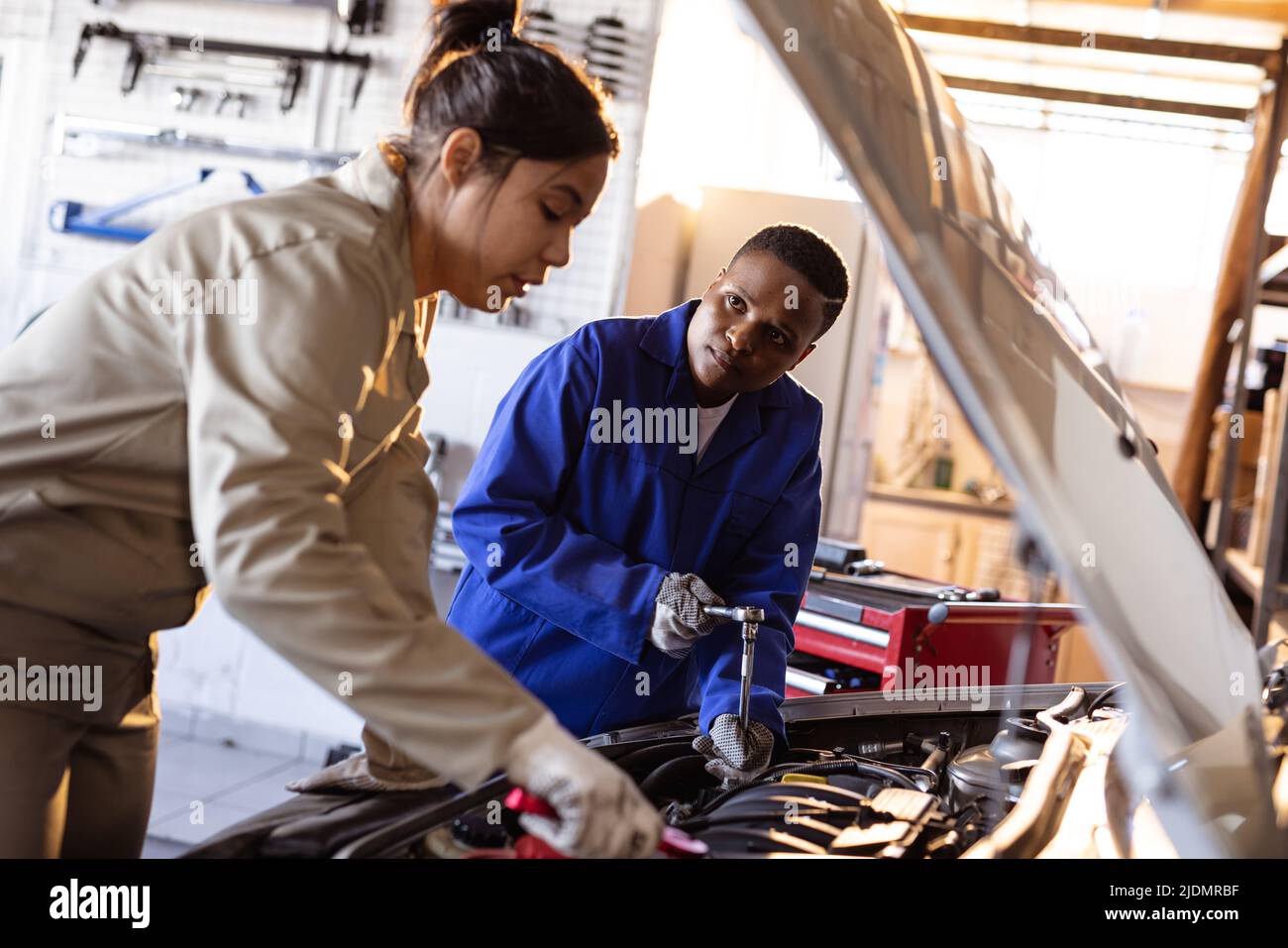 Mid adult multiracial female engineers repairing car's engine in workshop Stock Photo