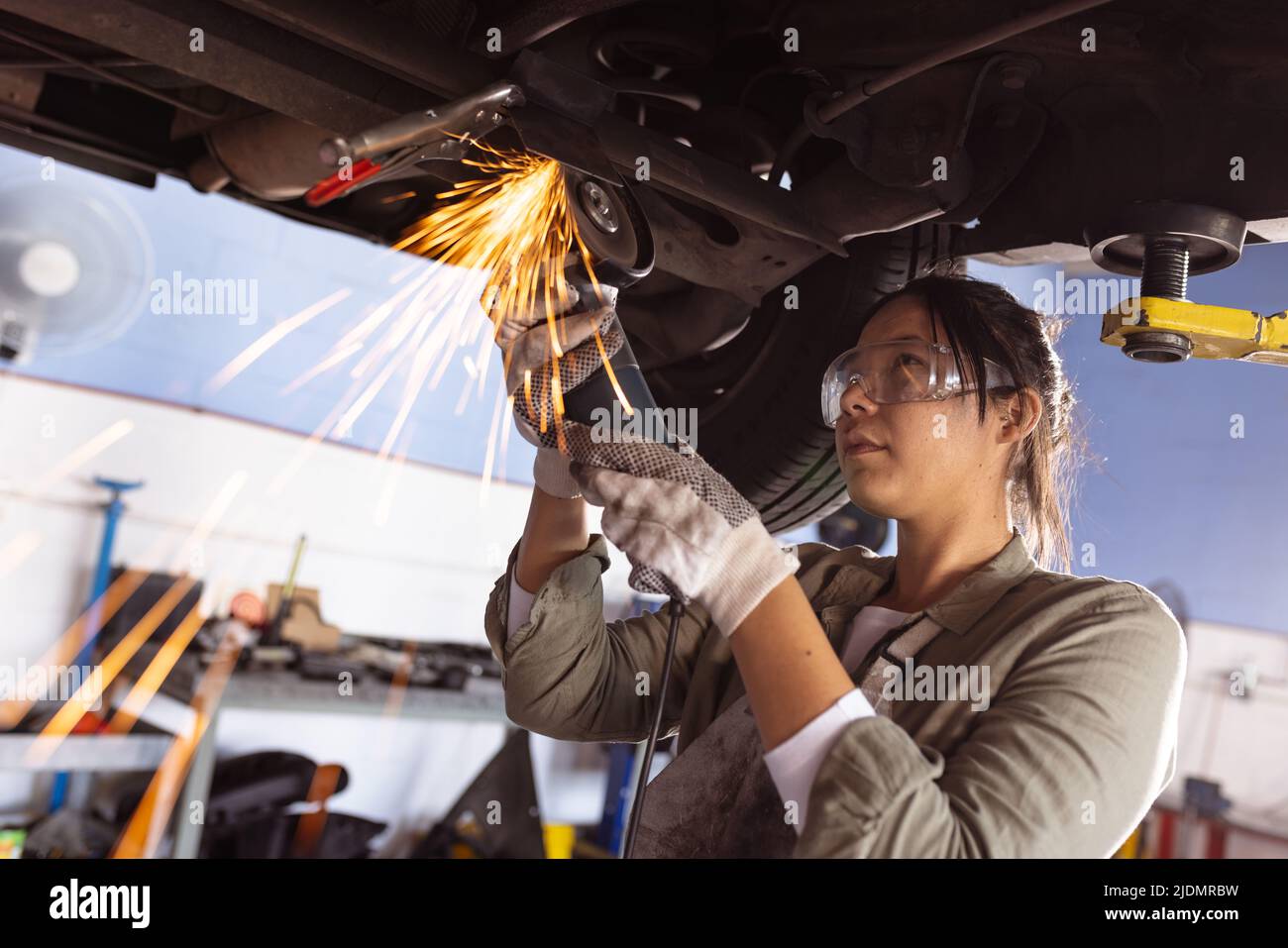 Mid adult asian female welder using work tool while repairing car in workshop Stock Photo