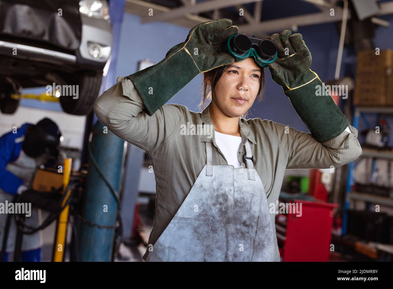Confident mid adult asian female welder wearing protective worker while working in workshop Stock Photo