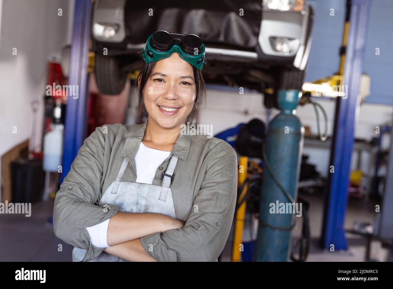 Portrait of smiling mid adult asian female welder with arms crossed standing in workshop Stock Photo