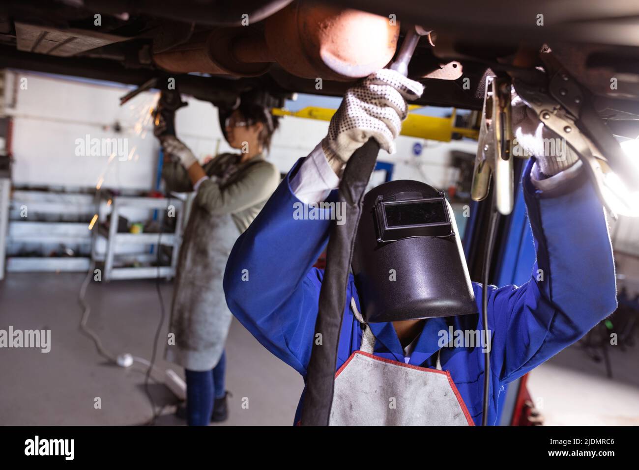 Mid adult multiracial female welders welding while repairing car under car lift in workshop Stock Photo