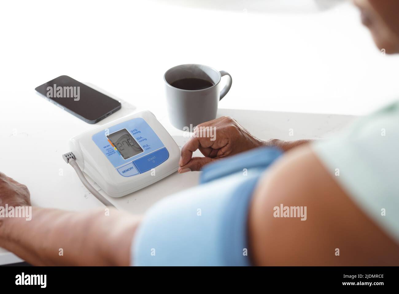 Cropped hand of african american senior woman checking blood pressure with gauge at kitchen island Stock Photo