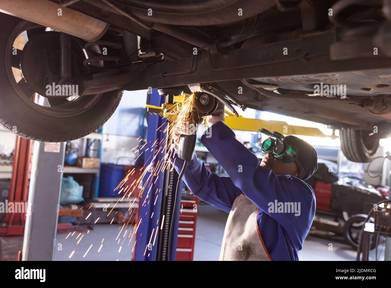 Mid adult african american female welder repairing car under car lift in workshop Stock Photo